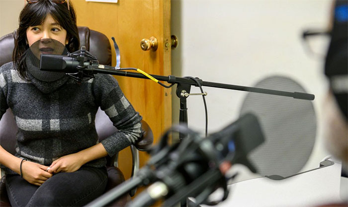 Faculty member sitting in makeshift studio with mic creating a podcast.