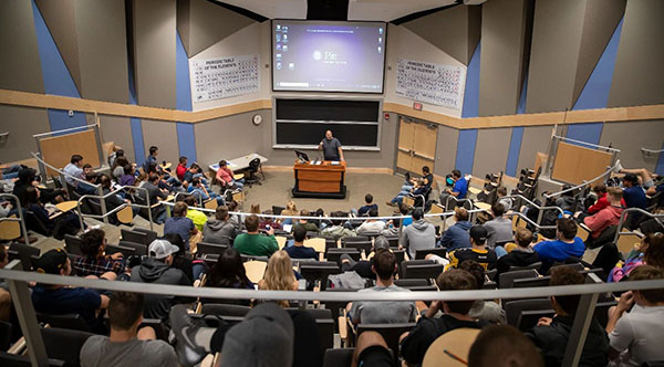 FAculty Member In Front Of A Large Class Lecturing.